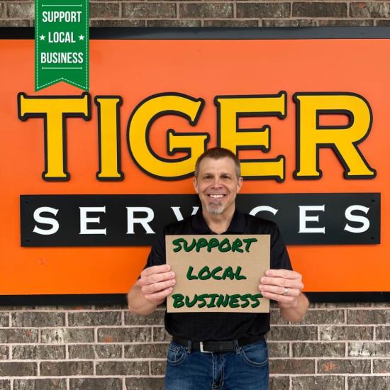 Smiling business owner holds Support Local Business sign.